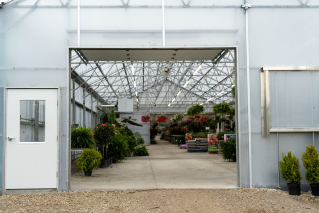 An entrance door and large overhead door at the rear of an a-frame retail greenhouse provide staff access and make it easy to load and unload plants and supplies.
