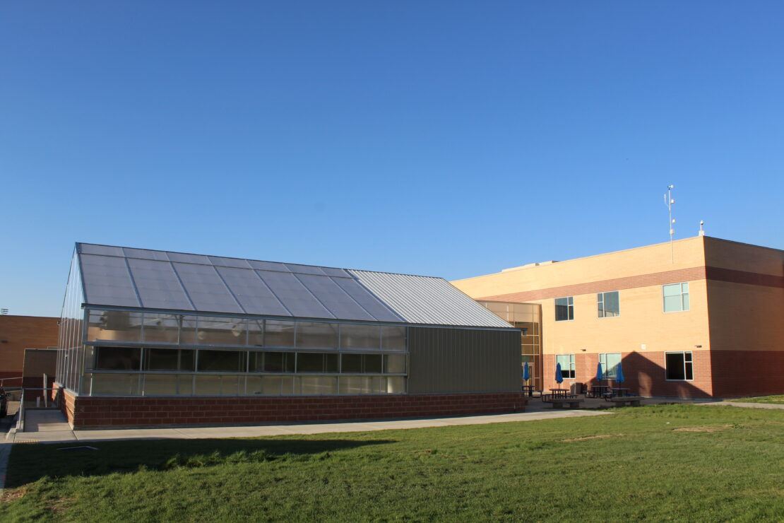 School greenhouse with diffused twin-wall polycarbonate covering on greenhouse roof and corrugated metal (insulated) on headhouse roof, gables, and sidewalls.